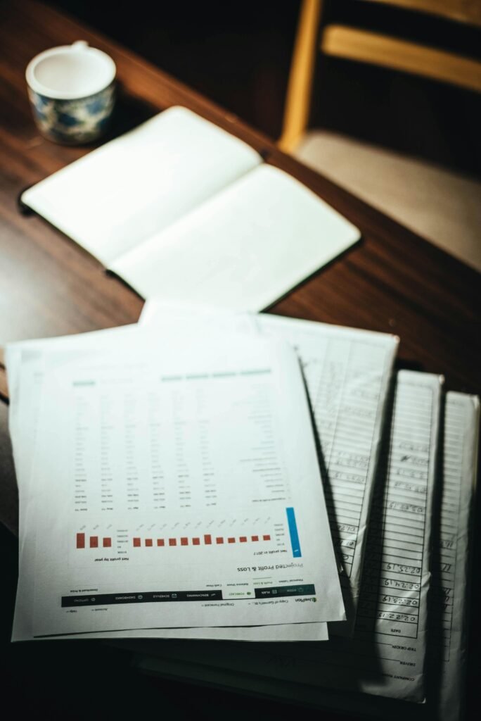 A desk featuring a stack of documents, an open notebook, and a mug of coffee under soft lighting.