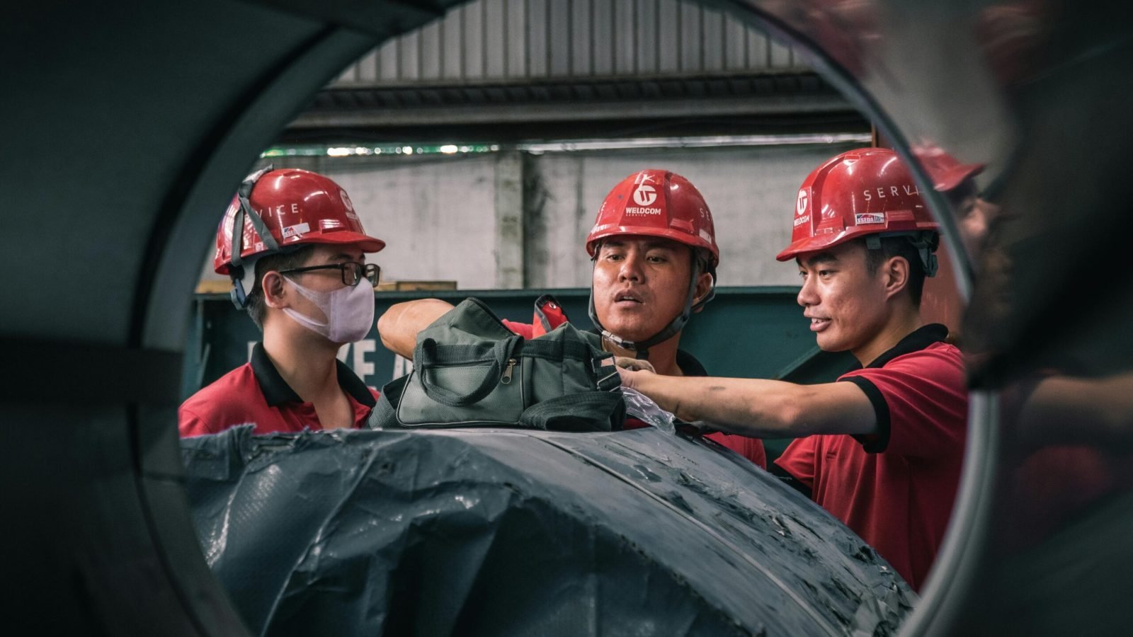 Three workers in safety helmets collaborate inside a factory setting, emphasizing teamwork and safety.